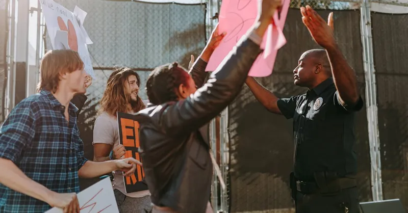 Protesters with signs confronting a police officer during a daytime demonstration.