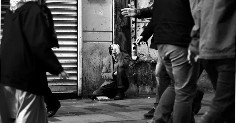 Black and white photo of an elderly man in distress, surrounded by pedestrians on a city street.
