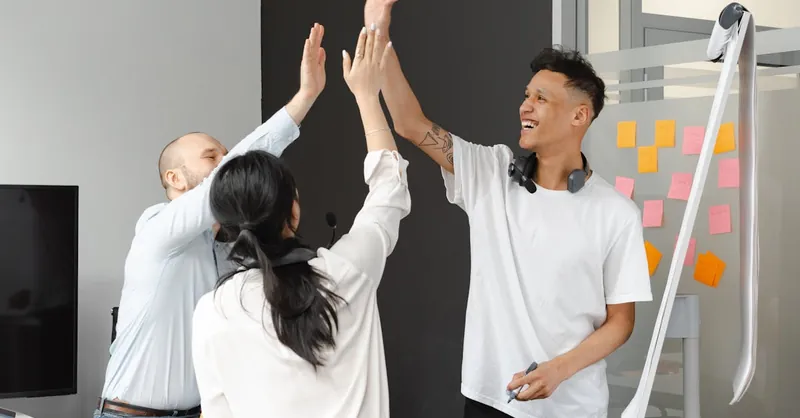 Diverse team members in an office high-fiving, symbolizing success and teamwork in a supportive environment.