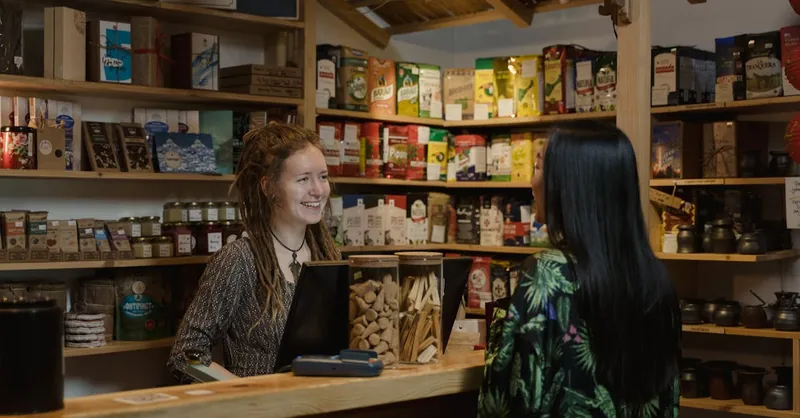 Friendly shopkeeper assisting a customer in a cozy, well-stocked store environment.