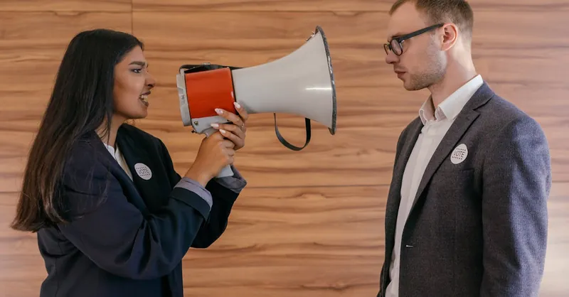 A woman using a megaphone to confront a man in a suit indoors, symbolizing political debate.