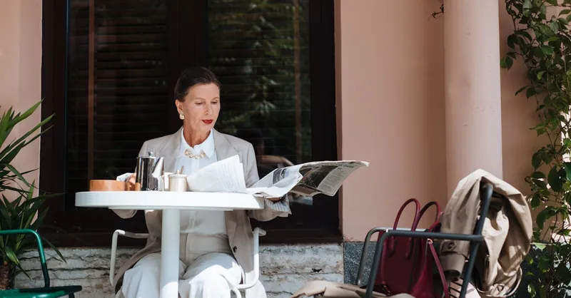 Sophisticated woman reading the newspaper outdoors, enjoying leisure at a stylish cafe.