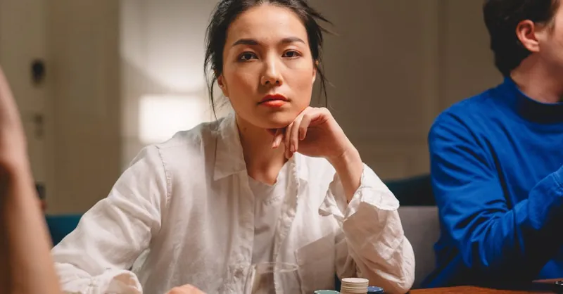 A thoughtful woman contemplating her next move at a poker game indoors.