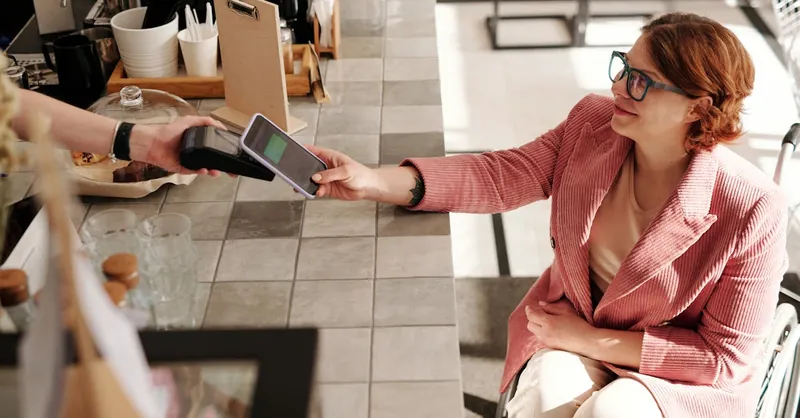 Woman in pink blazer making smartphone payment at a cafe from her wheelchair.