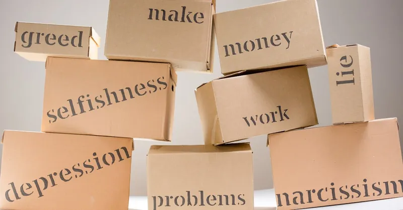 Stacked cardboard boxes displaying words like greed, depression, and problems, highlighting mental health themes.