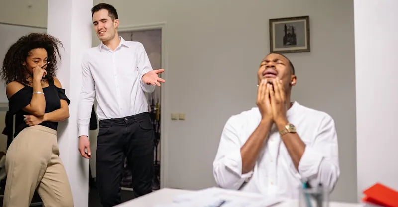 Three colleagues in an office setting display emotions of bullying and distress.