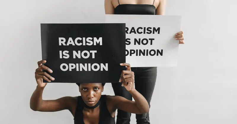 Two women holding signs with anti-racist slogans, emphasizing justice and community support.