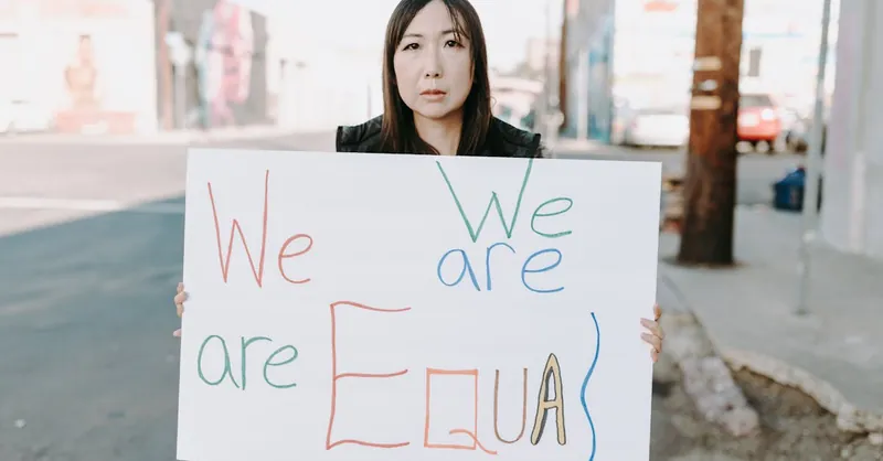 Empowering image of an Asian woman holding a sign promoting equality during a street protest.