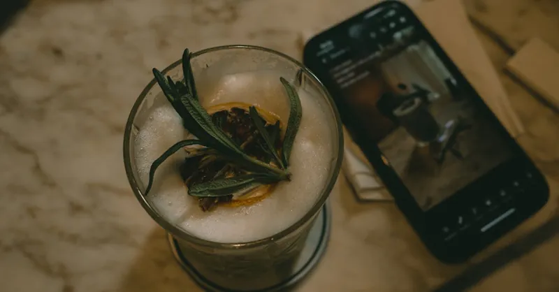 Close-up view of a matcha latte with garnish alongside a smartphone on a marble table, indoors.