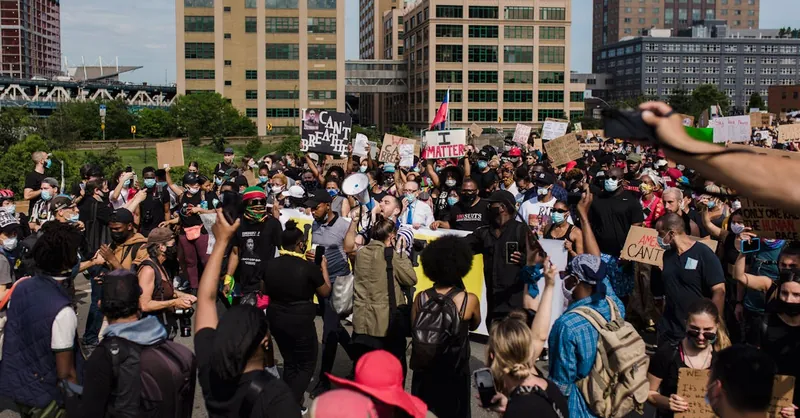 A large and diverse crowd gathers for a peaceful protest advocating for racial justice and equality in an urban setting.