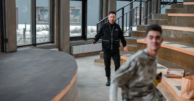 A security guard confronts a young man running indoors, depicting a tense moment.