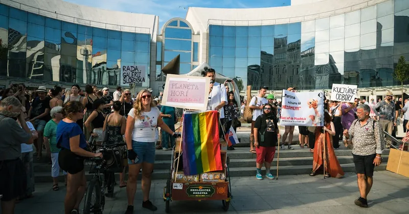 A peaceful protest in Bratislava featuring diverse participants with banners and a rainbow flag.