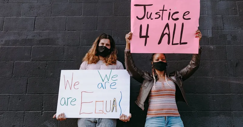 A diverse group of protesters holding equality and justice signs outdoors, wearing face masks for safety.