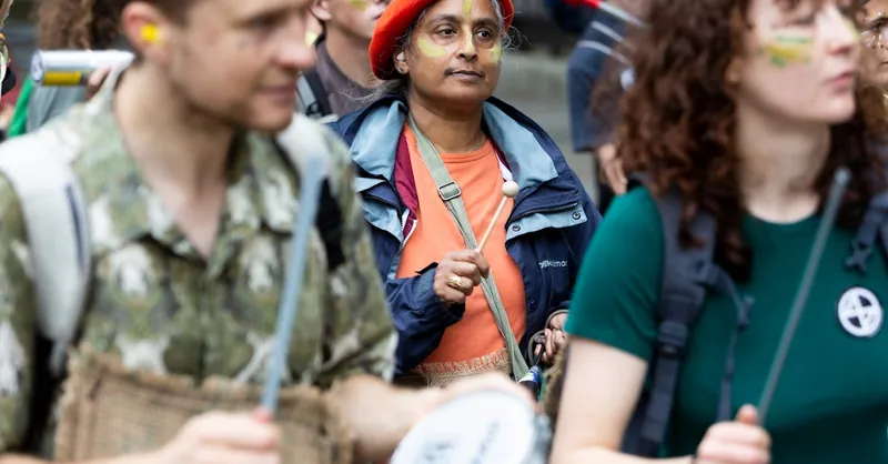 A dynamic street protest with diverse adult participants playing drums, showcasing activism.