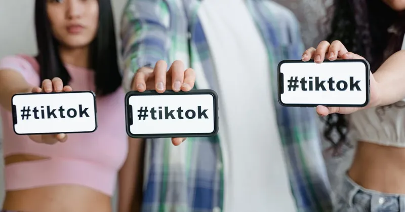 Young adults holding smartphones with TikTok hashtag, showcasing social media engagement.
