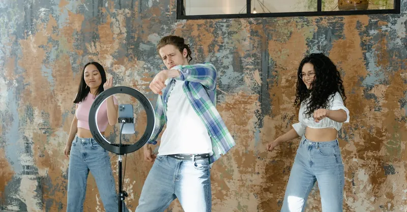 Group of friends dancing indoors with a smartphone and ring light setup for social media content.